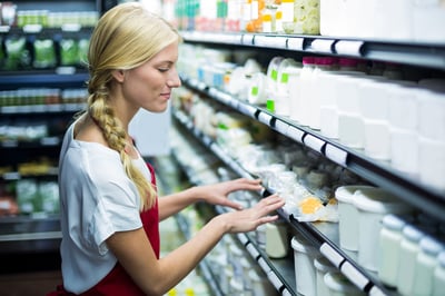 Female staff checking grocery products in shelf of supermarket